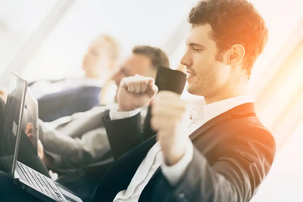 Üzletember és kollégái örülnek a pozitív pénzügyi eredményeknek egy tárgyalóban, a laptop képernyőjén növekedést mutató grafikon – sikeres szerkezetátalakítási eljárás után